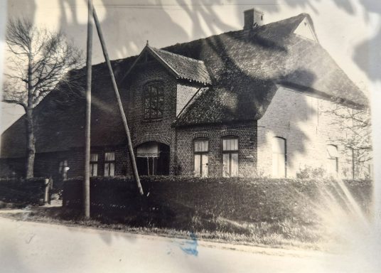 Historisches Haus mit Satteldach, umgeben von einem Garten und Bäumen.