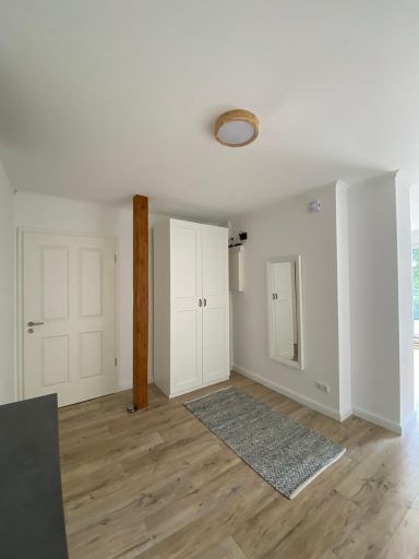 Heller Flur mit Holzfußboden, Spiegel, weißen Wänden und moderner Deckenleuchte.