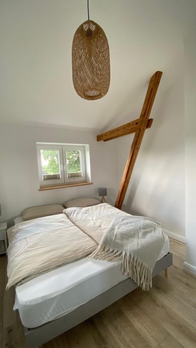 Helles Schlafzimmer mit einem großen Bett, Holzstruktur und eleganter Deckenlampe.