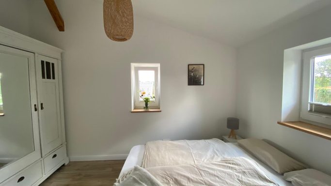 Helles Schlafzimmer mit Bett, Schrank, Fenster und moderner Dekoration.