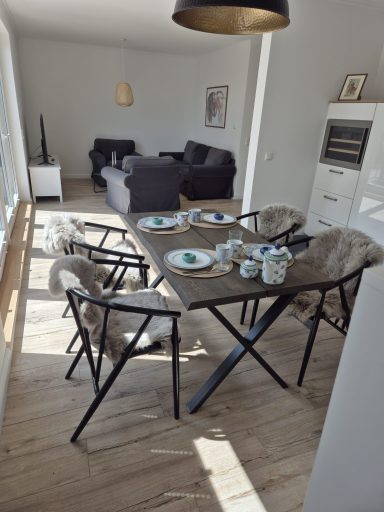 Ein helles Esszimmer mit einem Tisch, Geschirr und einer Sitzgruppe im Hintergrund.