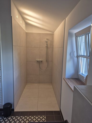 Moderne Duschkabine mit Fliesen und Fenster, helle Beleuchtung.