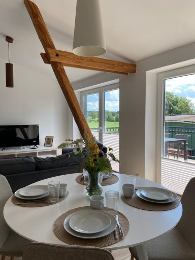 Essbereich mit rundem Tisch, Geschirr, Blumen und schwarzem Fernseher im Hintergrund.