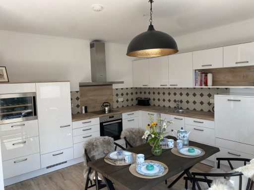 Moderne Küche mit weißen Schränken, Holztisch und frischen Blumen.