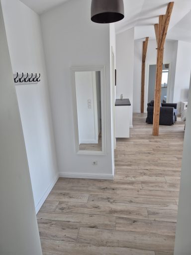 Heller Flur mit Holzfußboden, Spiegel, Garderobe und offenen Wohnbereich im Hintergrund.