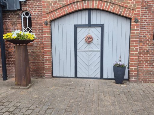 Graue Holzscheune mit einer Dekoration, umgeben von Blumen und einem Topf.