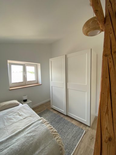 Helles Schlafzimmer mit einem weißen Kleiderschrank und einem Bett neben einem Fenster.