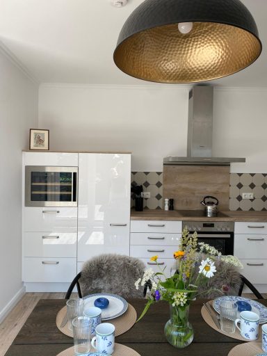 Moderne Küche mit Esstisch, Blumenstrauß und eleganter Deckenlampe.