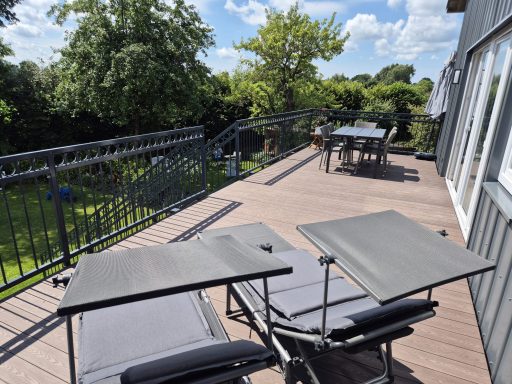 Terrasse mit zwei Tischen, Blick ins Grüne und sonnigem Himmel.