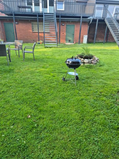 Grill auf Rasen in einem Garten mit Sitzgelegenheiten und einem Feuerplatz.