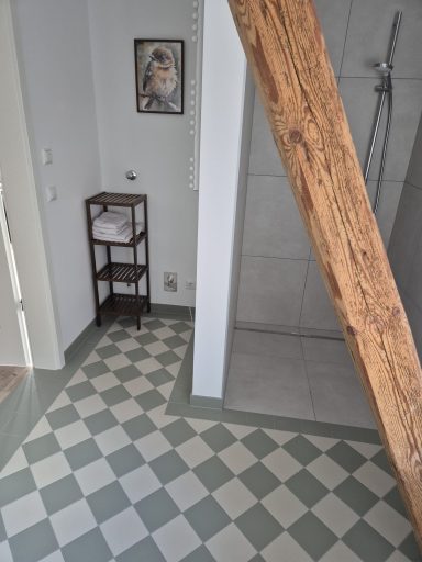 Badezimmer mit Fliesenboden, Dusche und einem Regal mit Handtüchern.