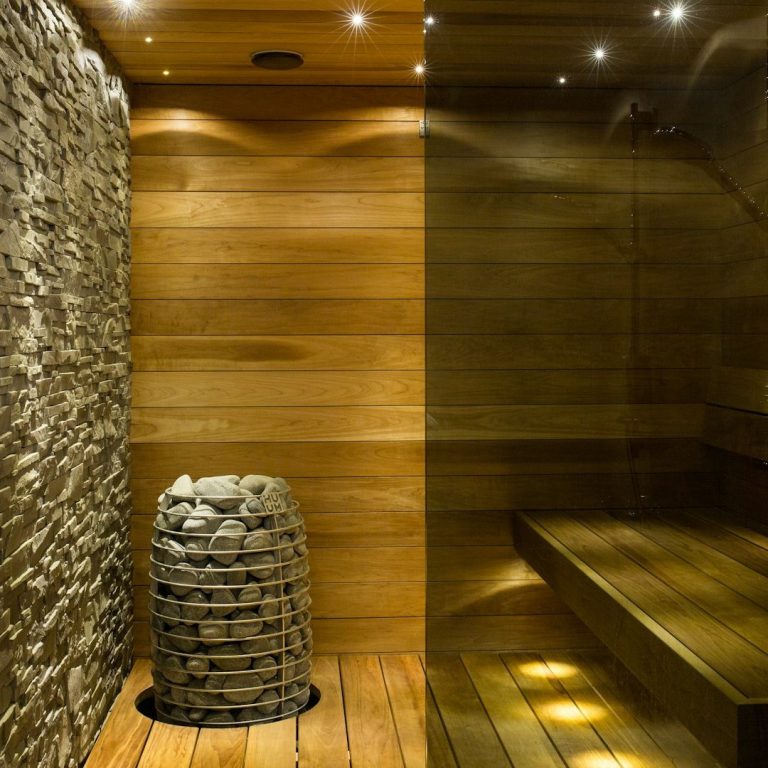 Moderne Sauna mit Holzverkleidung, Steinbrunnen und gedämpfter Beleuchtung.