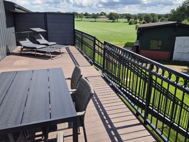 Terrasse mit Tisch und Stühlen, Blick auf einen grünen Rasen und eine Gartenhütte.