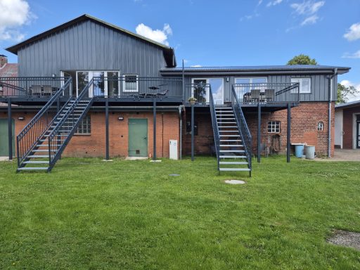 Zweistöckiges Gebäude mit zwei Außentreppen und grüner Rasenfläche.