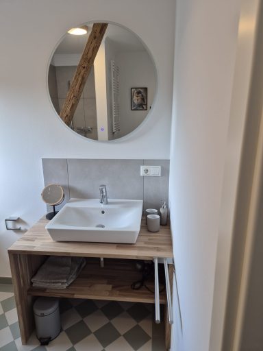 Moderne Waschtisch mit runder Spiegel, Holzregal und Waschbecken in einem Badezimmer.