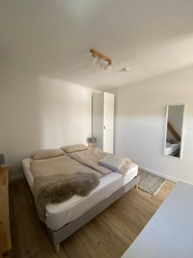 Helles Schlafzimmer mit Doppelbett, Spiegel und Holzfußboden.