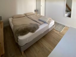 Helles Schlafzimmer mit Doppelbett, Teppich, Kommode und Spiegel.