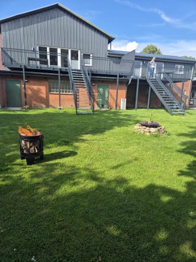 Hinterhof mit grünem Rasen, Feuerschale und einem zweigeschossigen Gebäude.