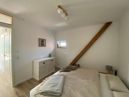 Helles Schlafzimmer mit einem Bett, Schrank und einem schrägen Holzbalken.
