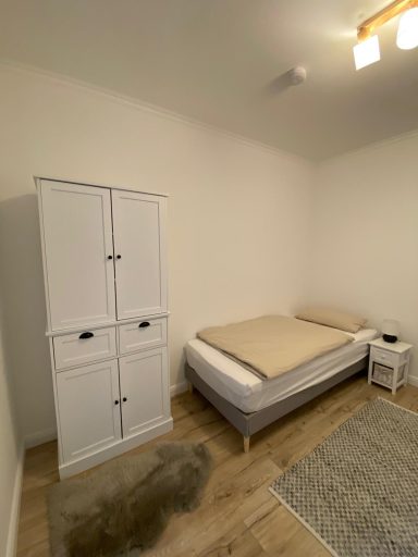 Ein einfaches Schlafzimmer mit Bett, Nachttisch und einem weißen Schrank.