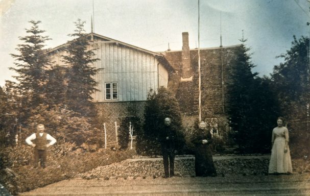 Historisches Foto von vier Personen vor einem großen, alten Gebäude und Bäumen.