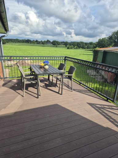 Terrasse mit Tisch, Stühlen und Blick auf eine Wiese unter bewölktem Himmel.
