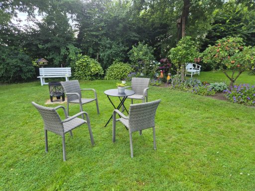 Garten mit Rasen, Stühlen, Tisch und bunten Blumenbeeten im Hintergrund.
